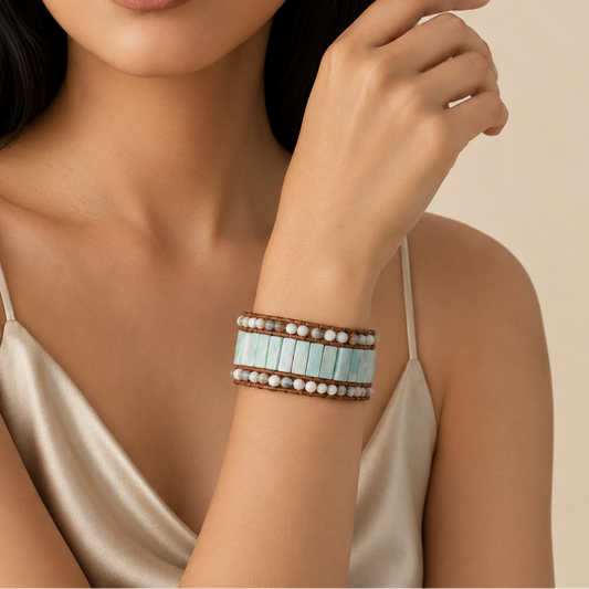 Close-up of a woman's arm wearing a bracelet with turquoise stones and brown leather straps on a beige background.