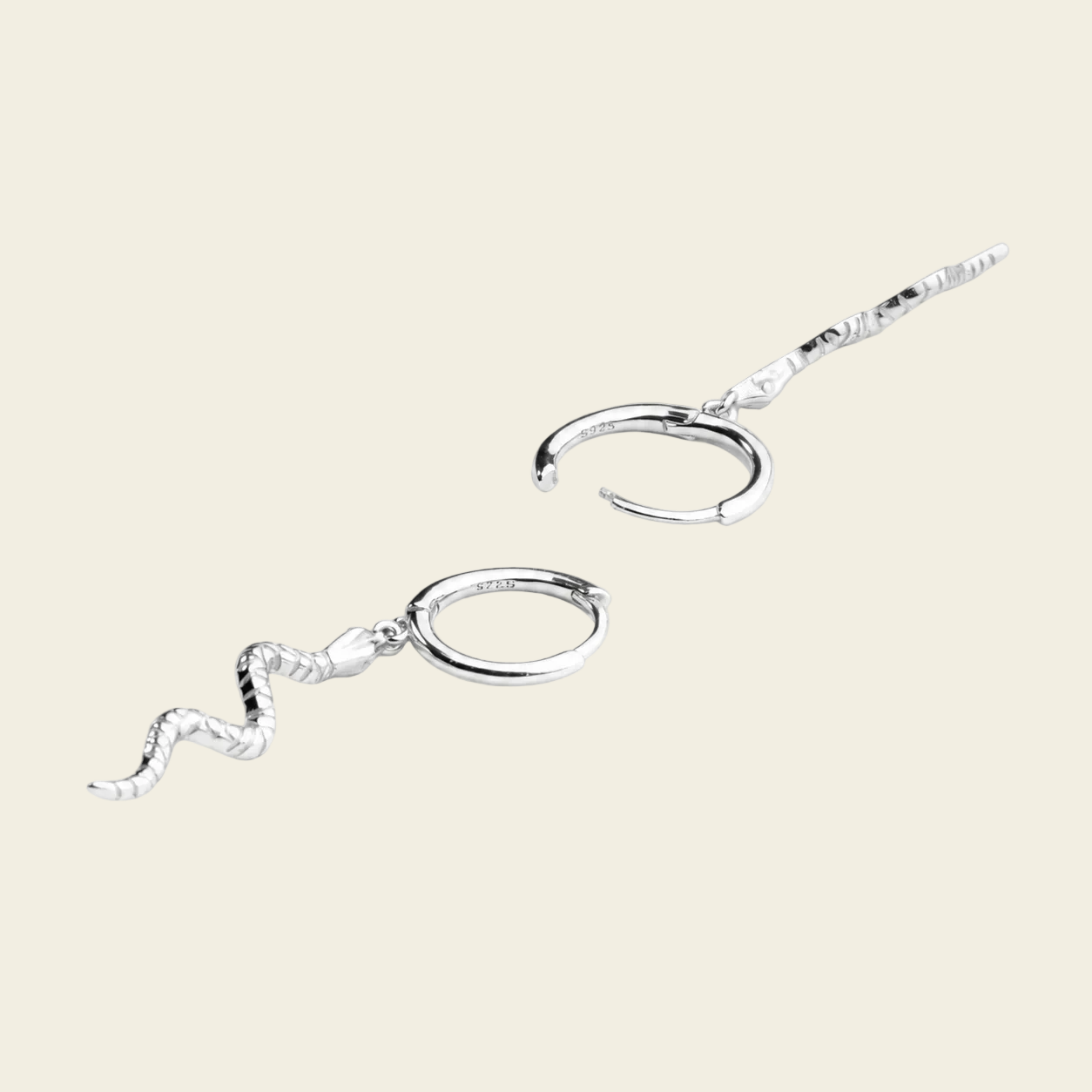 A pair of silver-toned ear cuffs with textured wavy dangling chains, displayed on a solid light beige background.