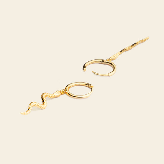 Gold snake-shaped earrings on a beige background
