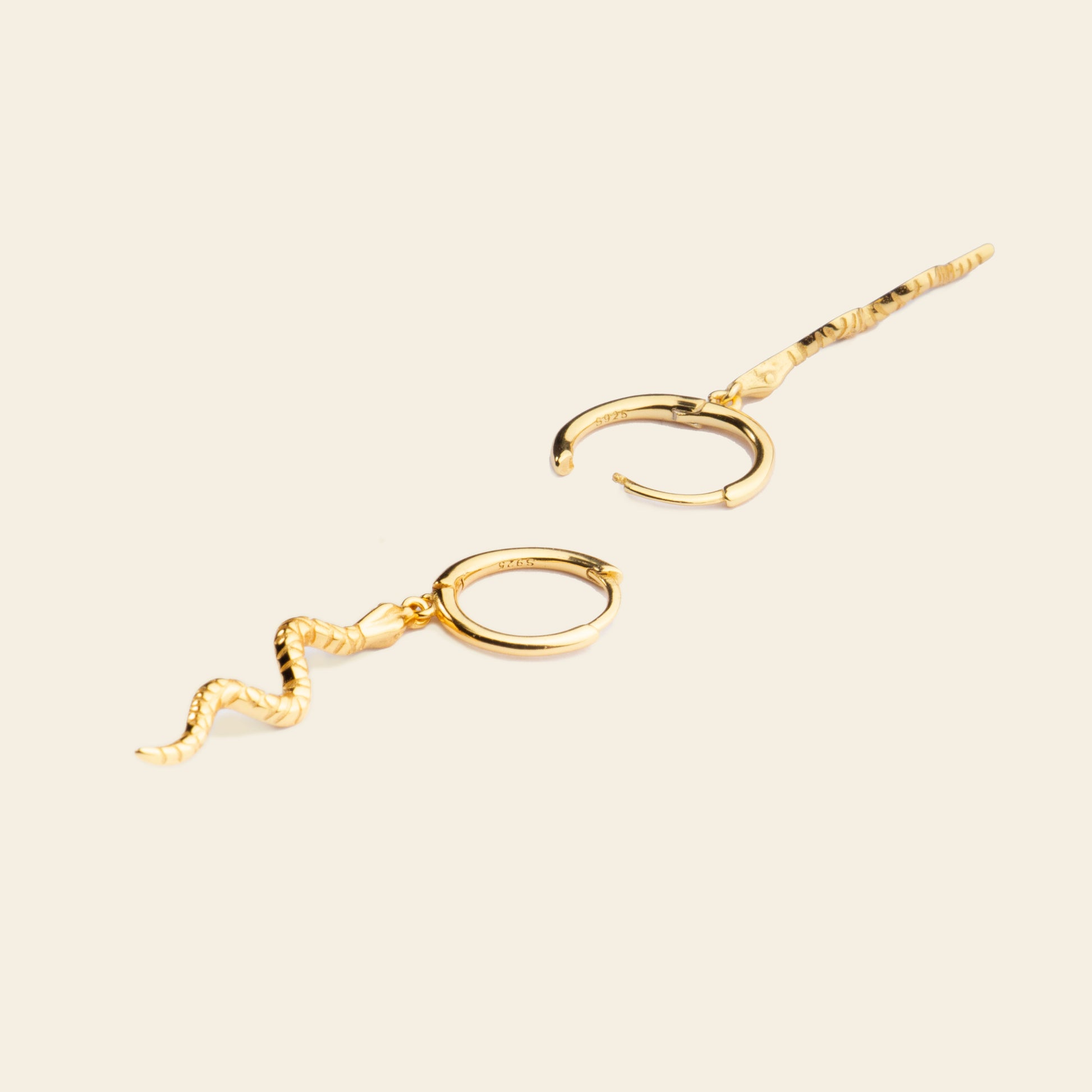 Gold snake-shaped earrings on a beige background