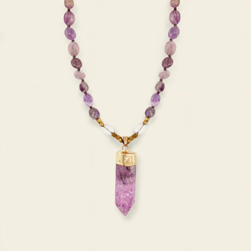 Necklace with purple beaded chain and a pink crystal pendant on a beige background