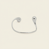 A minimalist silver open cuff bracelet with a curved, organic teardrop-shaped end, shown on a light cream background.