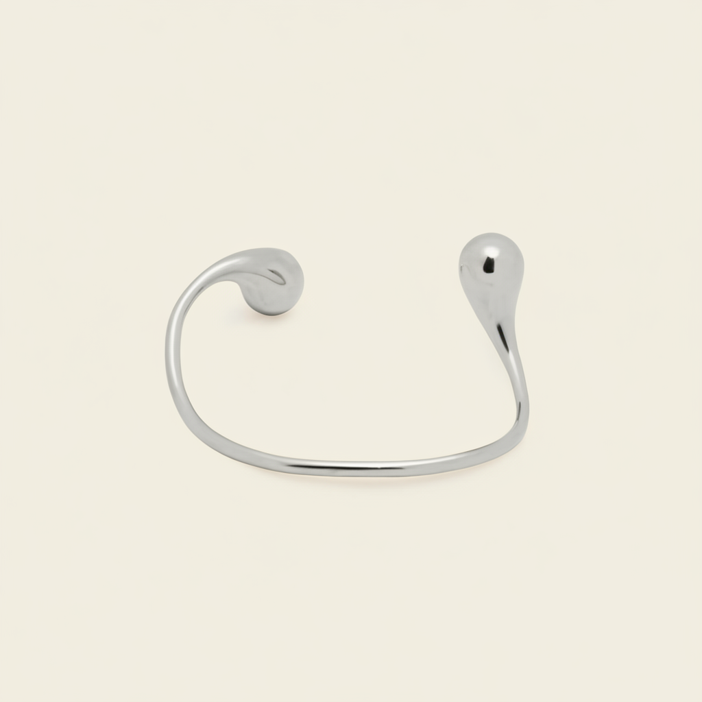 A minimalist silver open cuff bracelet with a curved, organic teardrop-shaped end, shown on a light cream background.