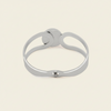 A polished silver-toned metal cuff bracelet with a unique openwork design and a small sliding clasp, shown on a solid light beige background.