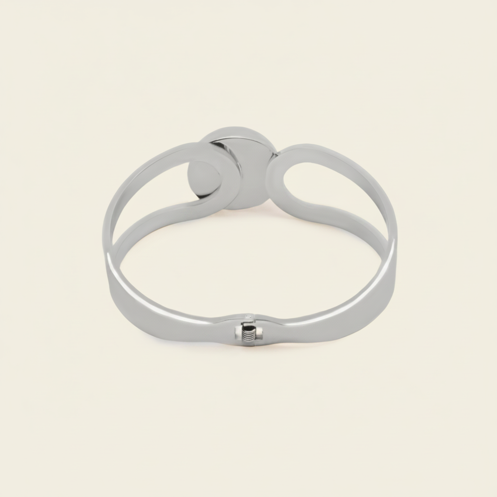 A polished silver-toned metal cuff bracelet with a unique openwork design and a small sliding clasp, shown on a solid light beige background.