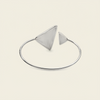 A silver-toned open bangle bracelet with two triangular geometric charms, displayed on a light cream background.