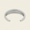 A polished silver open cuff bangle bracelet, photographed on a clean, solid, warm off-white background.