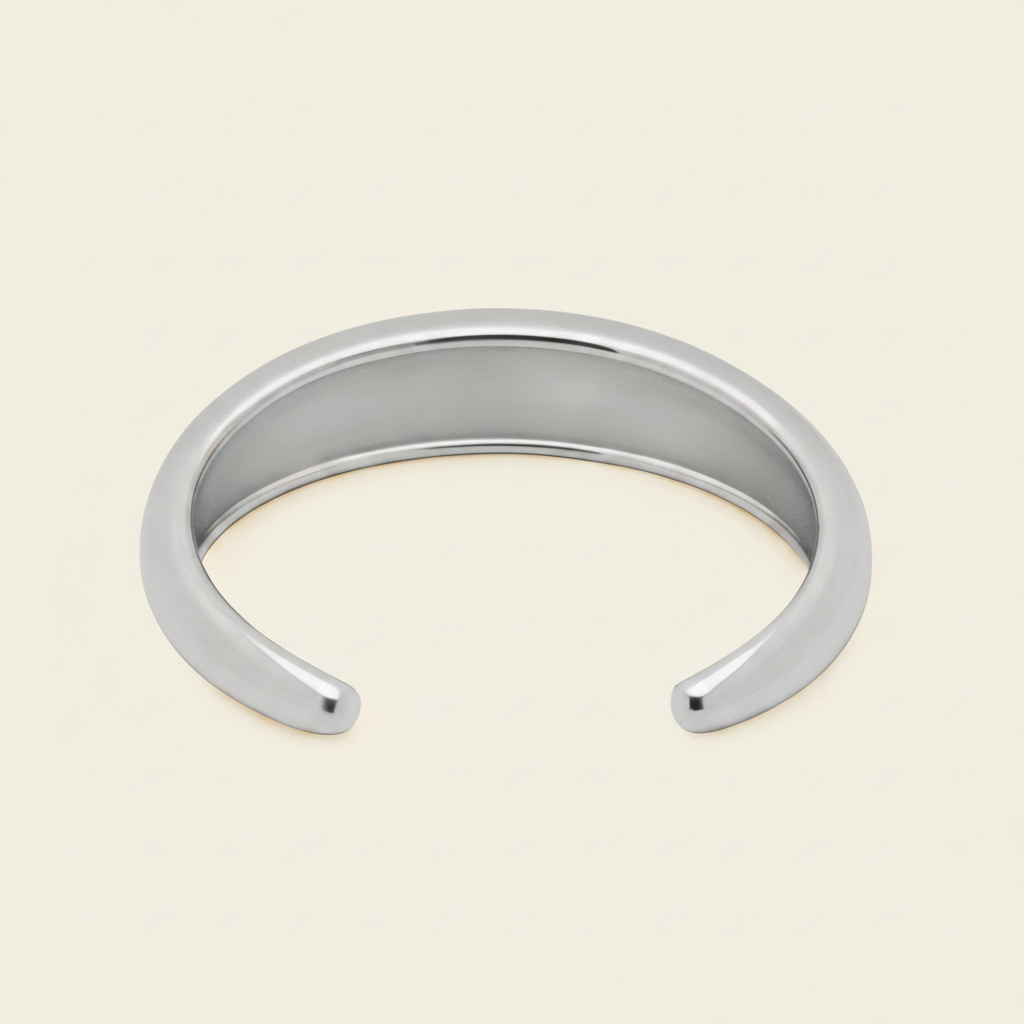 A polished silver open cuff bangle bracelet, photographed on a clean, solid, warm off-white background.