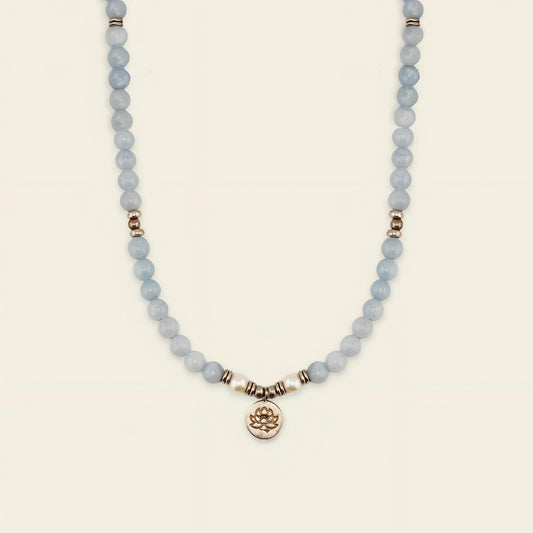Necklace with light blue beads and a gold charm on a beige background