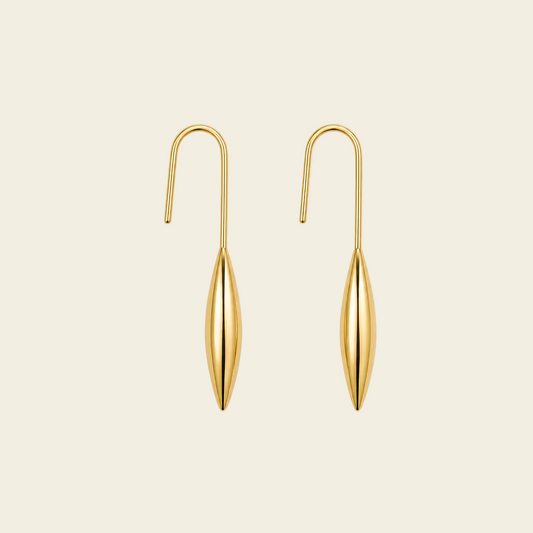 A pair of gold drop earrings with a curved hook back and a teardrop-shaped dangling pendant, shown on a solid light beige background.