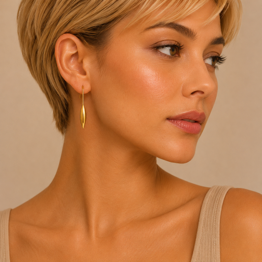 A close-up of a woman with short blonde hair wearing a delicate gold dangle earring, shown in profile against a warm beige background.