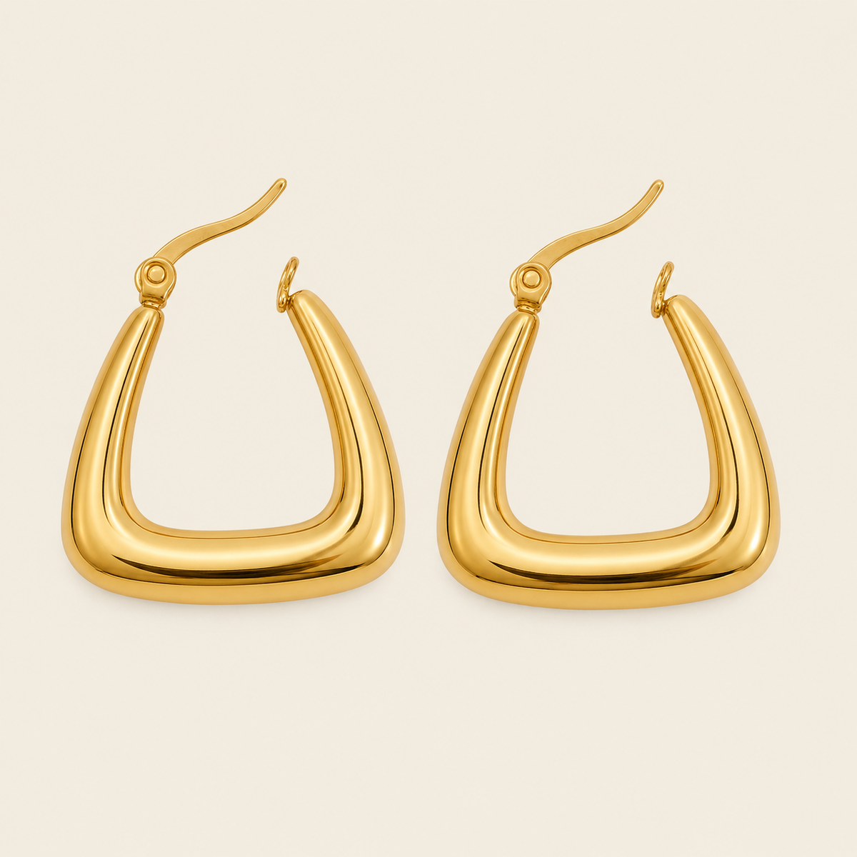 A pair of chunky, polished gold hoop earrings with a modern, curved triangular shape, displayed on a solid light beige background.