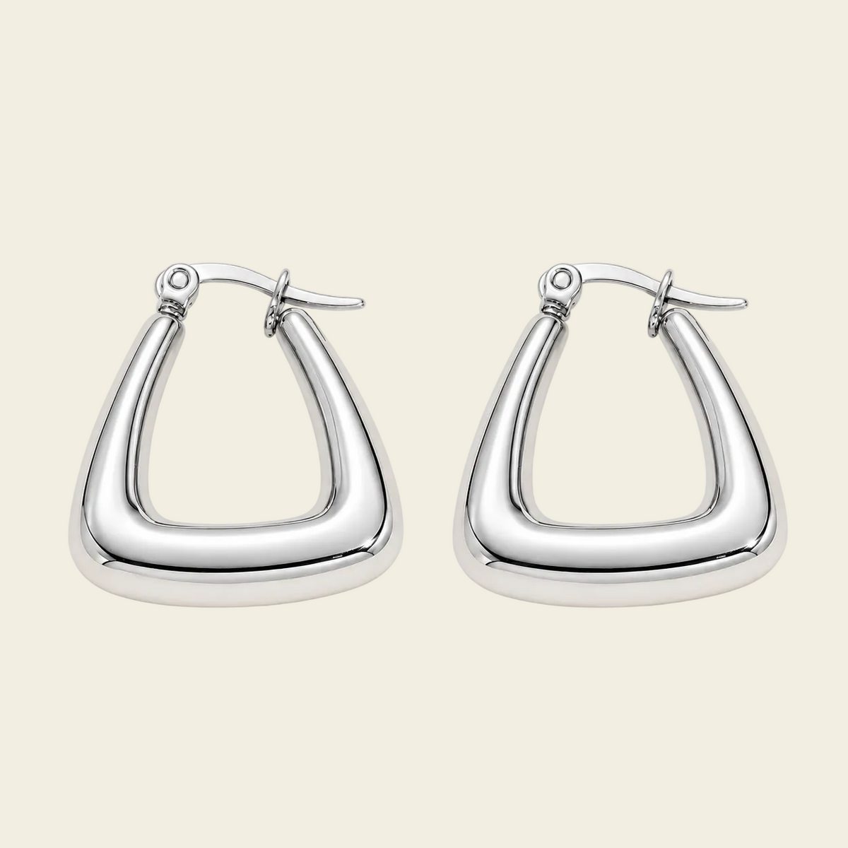 A pair of polished silver-tone geometric hoop earrings with a thick, rounded triangular shape, displayed on a solid light beige background.
