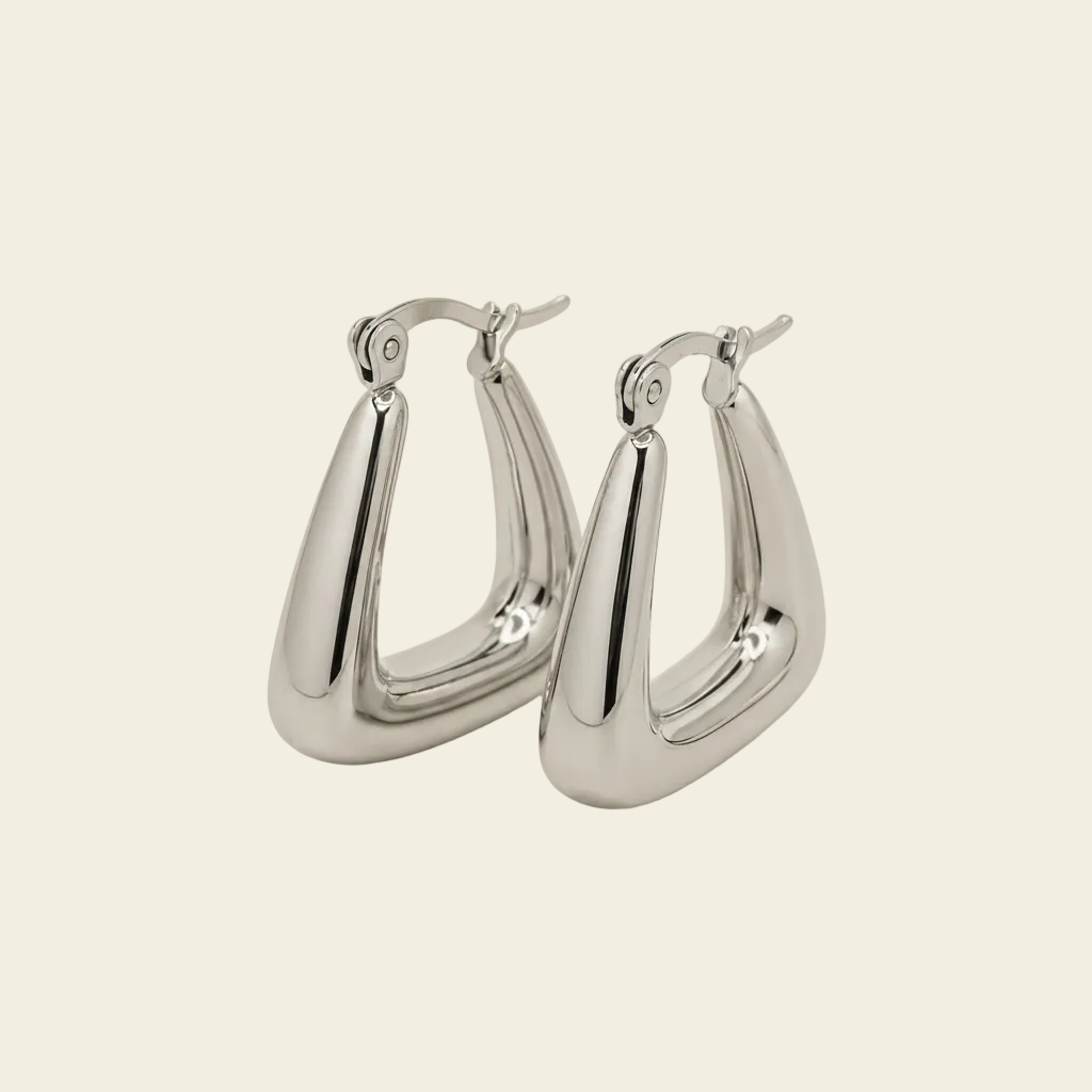 A pair of polished silver-tone hoop earrings with a unique curved, teardrop-like shape and fishhook backings, displayed on a solid light beige background.