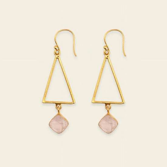 Gold triangle earrings with pink stone drops on a beige background