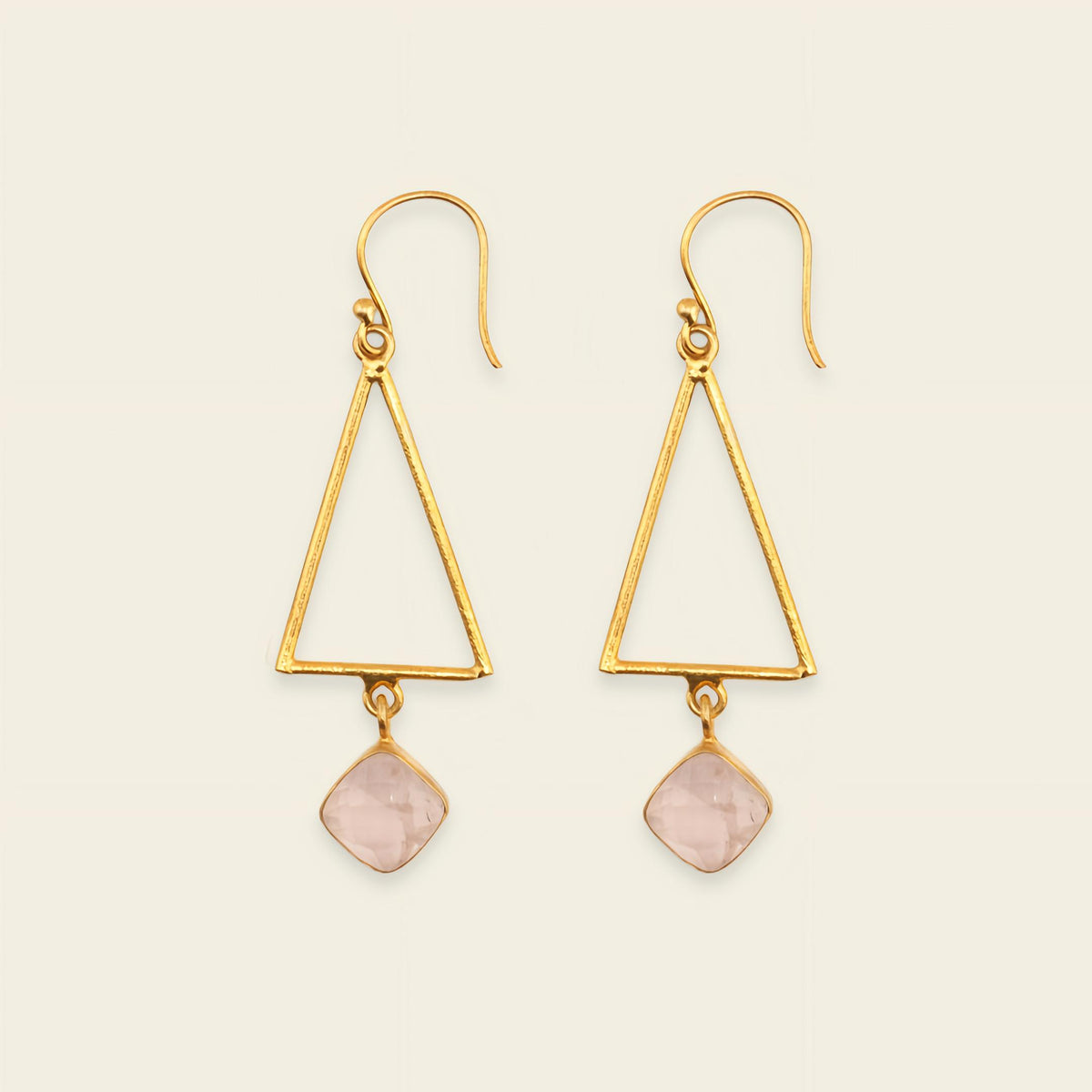 Gold triangle earrings with pink stone drops on a beige background