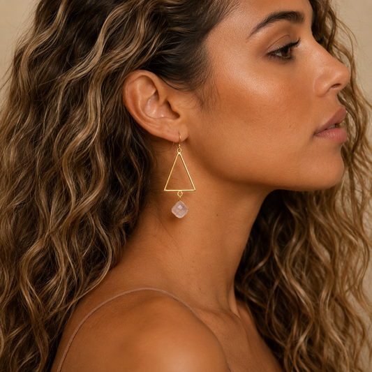 Close-up of a woman wearing a gold triangle earring with a pearl drop.
