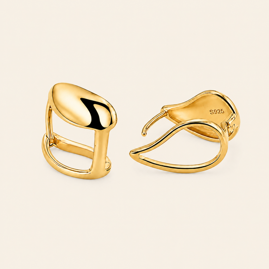 A pair of polished yellow gold huggie hoop earrings shown on a warm off-white background.