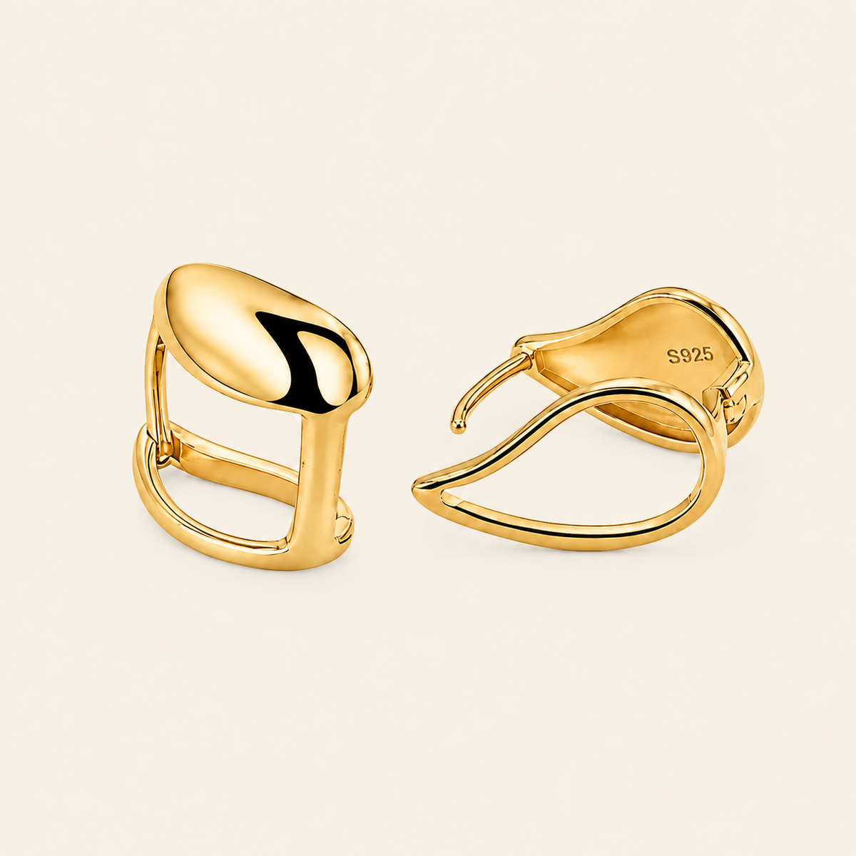 A pair of polished yellow gold huggie hoop earrings shown on a warm off-white background.