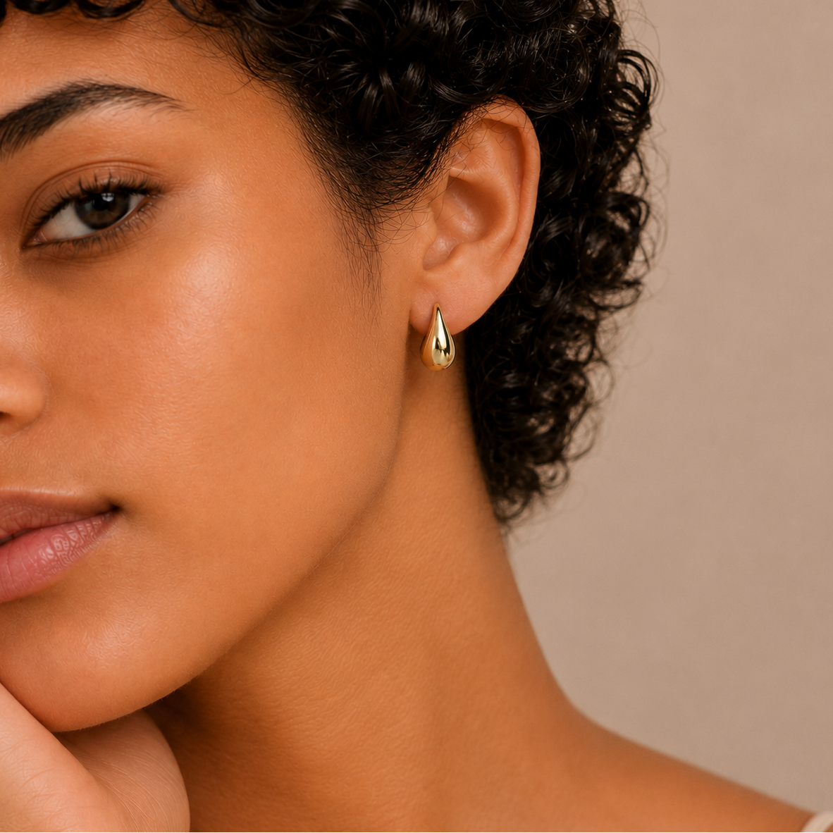 Close-up of a woman wearing a gold earring with a neutral background