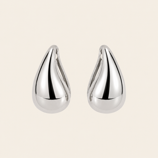 Pair of silver teardrop earrings on a beige background