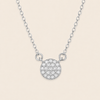 A silver chain necklace featuring a round pavé pendant with a textured, glittering surface, displayed against a solid light beige background.