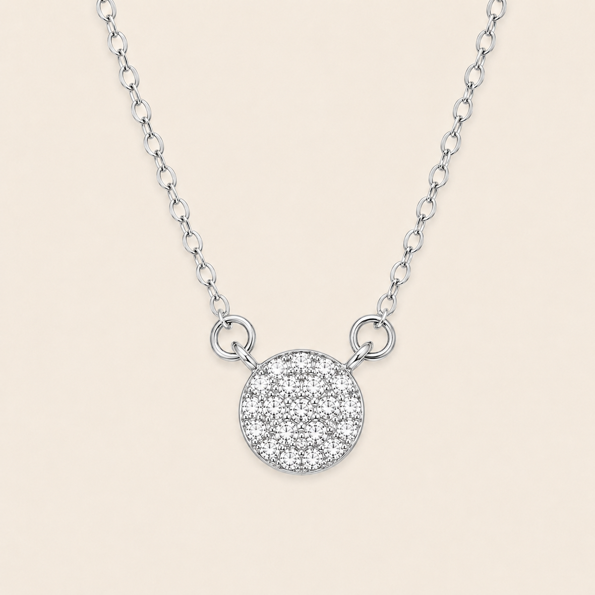 A silver chain necklace featuring a round pavé pendant with a textured, glittering surface, displayed against a solid light beige background.