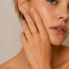 Woman wearing a gold ring with a diamond on a neutral background