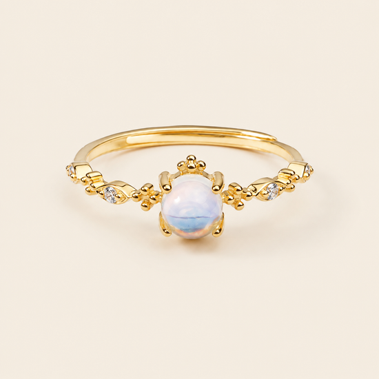 Gold ring with a central white gemstone on a beige background