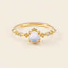 Gold ring with a central white gemstone on a beige background