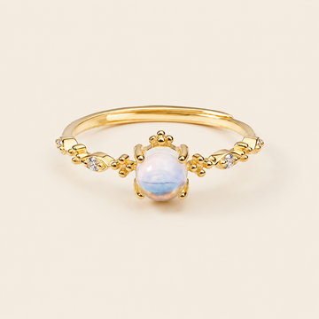 Gold ring with a central white gemstone on a beige background