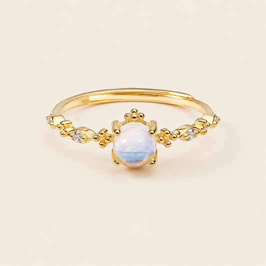 Gold ring with a central white gemstone on a beige background