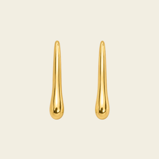 A pair of gold teardrop-shaped stud earrings with a polished, reflective finish, displayed on a solid light beige background.