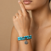 Turquoise beaded bracelet with a silver charm on a person's wrist against a beige background