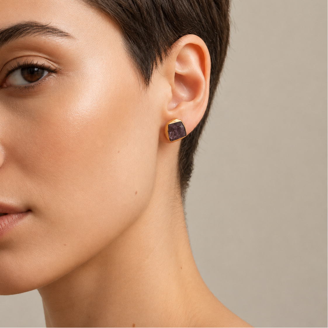 Close-up of a woman wearing a purple earring against a neutral background