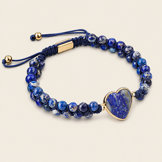 A beaded bracelet featuring deep blue and white marbled beads, a dark blue cord adjustable slider with gold-tone metal accents, and a polished heart-shaped blue stone charm set in gold-tone metal, displayed on a light beige background.