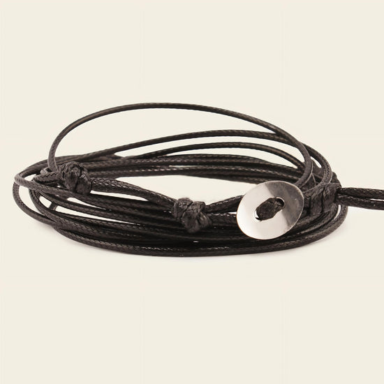 Black cord bracelet with a silver disc charm on a beige background