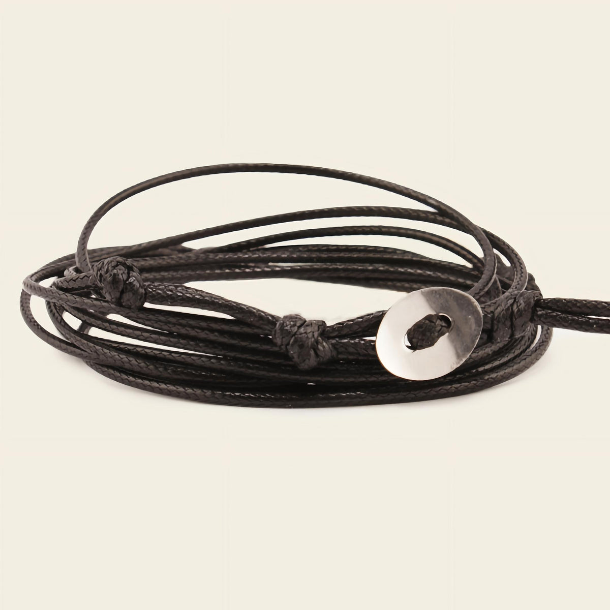 Black cord bracelet with a silver disc charm on a beige background