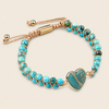 A turquoise and gold beaded bracelet with a heart-shaped turquoise centerpiece, displayed on a light beige background.