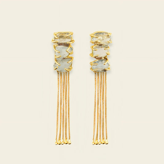 Gold earrings with gemstones and chains on a beige background