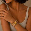 Woman wearing a beige tank top and multiple bracelets on her wrist against a neutral background