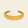 A polished gold open cuff bracelet, also known as a hinged bangle, shown on a solid light beige background.