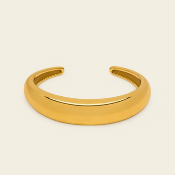 A polished gold open cuff bracelet, also known as a hinged bangle, shown on a solid light beige background.