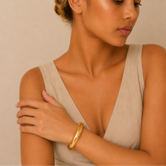 Woman wearing a beige sleeveless top and gold bracelet against a beige background