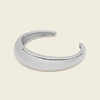 A polished silver open cuff bracelet, also known as a hinged bangle, shown on a solid light beige background.