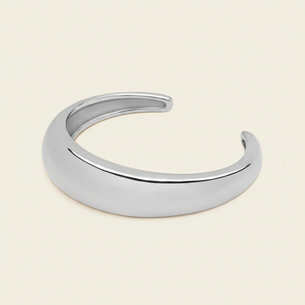 A polished silver open cuff bracelet, also known as a hinged bangle, shown on a solid light beige background.