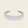 A polished silver open cuff bracelet, also known as a hinged bangle, shown on a solid light beige background.