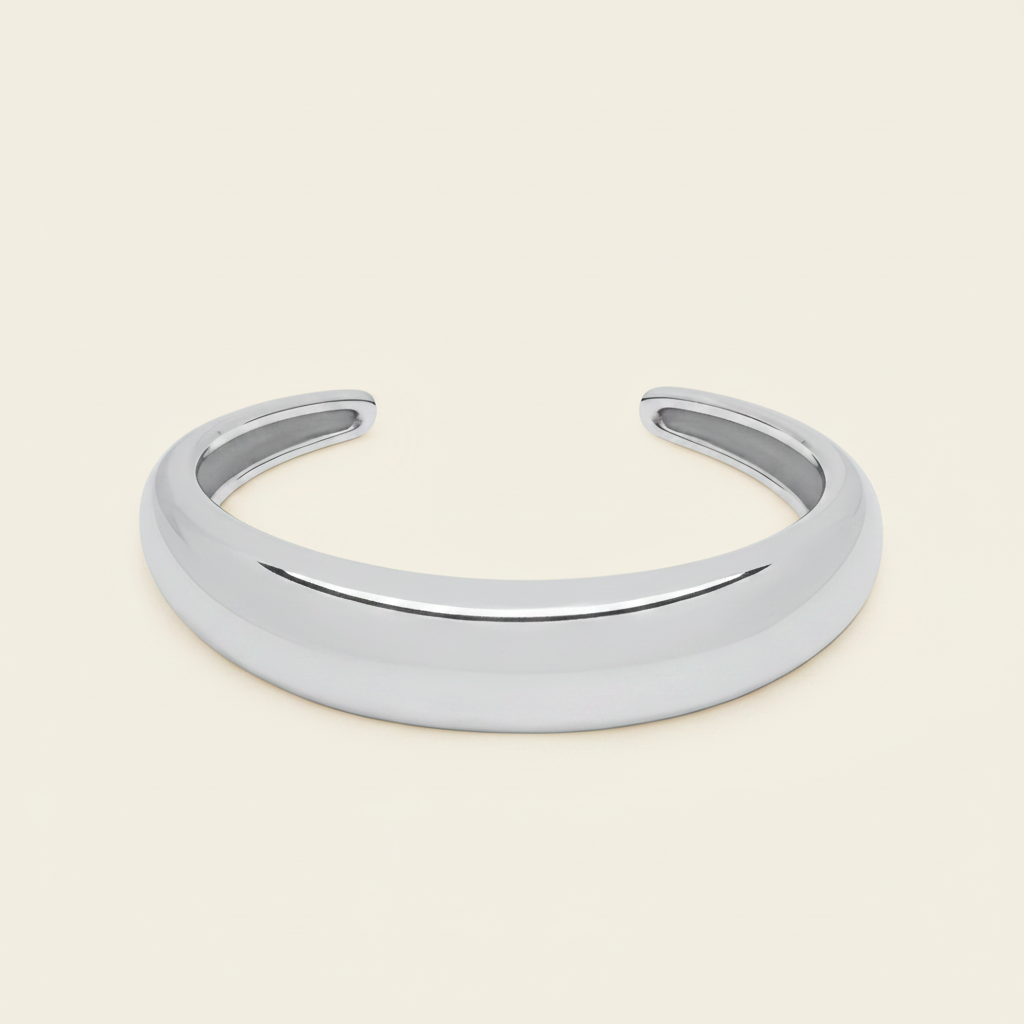 A polished silver open cuff bracelet, also known as a hinged bangle, shown on a solid light beige background.
