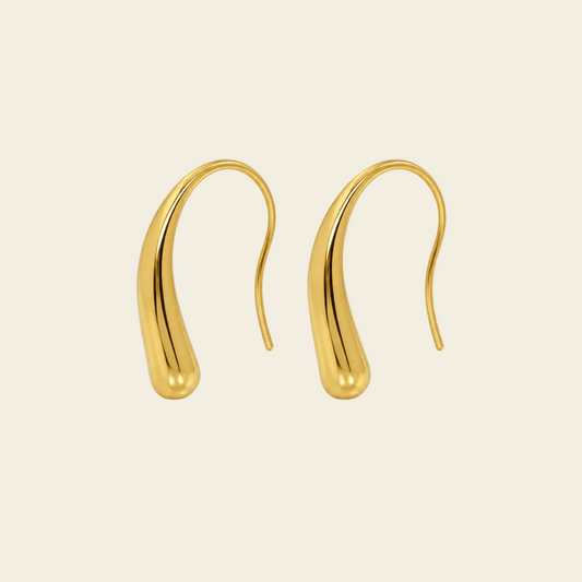 A pair of gold teardrop-shaped dangle earrings with smooth, polished curves, displayed on a solid cream-colored background.