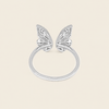 A silver butterfly ring with two delicate wing motifs on a smooth band, set against a solid light beige background.